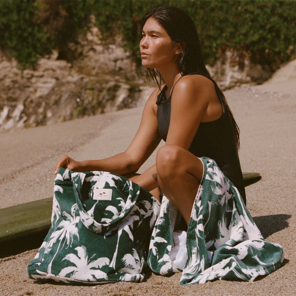 Terry tote bag with palm tree print towel and surfboard, beach setting.