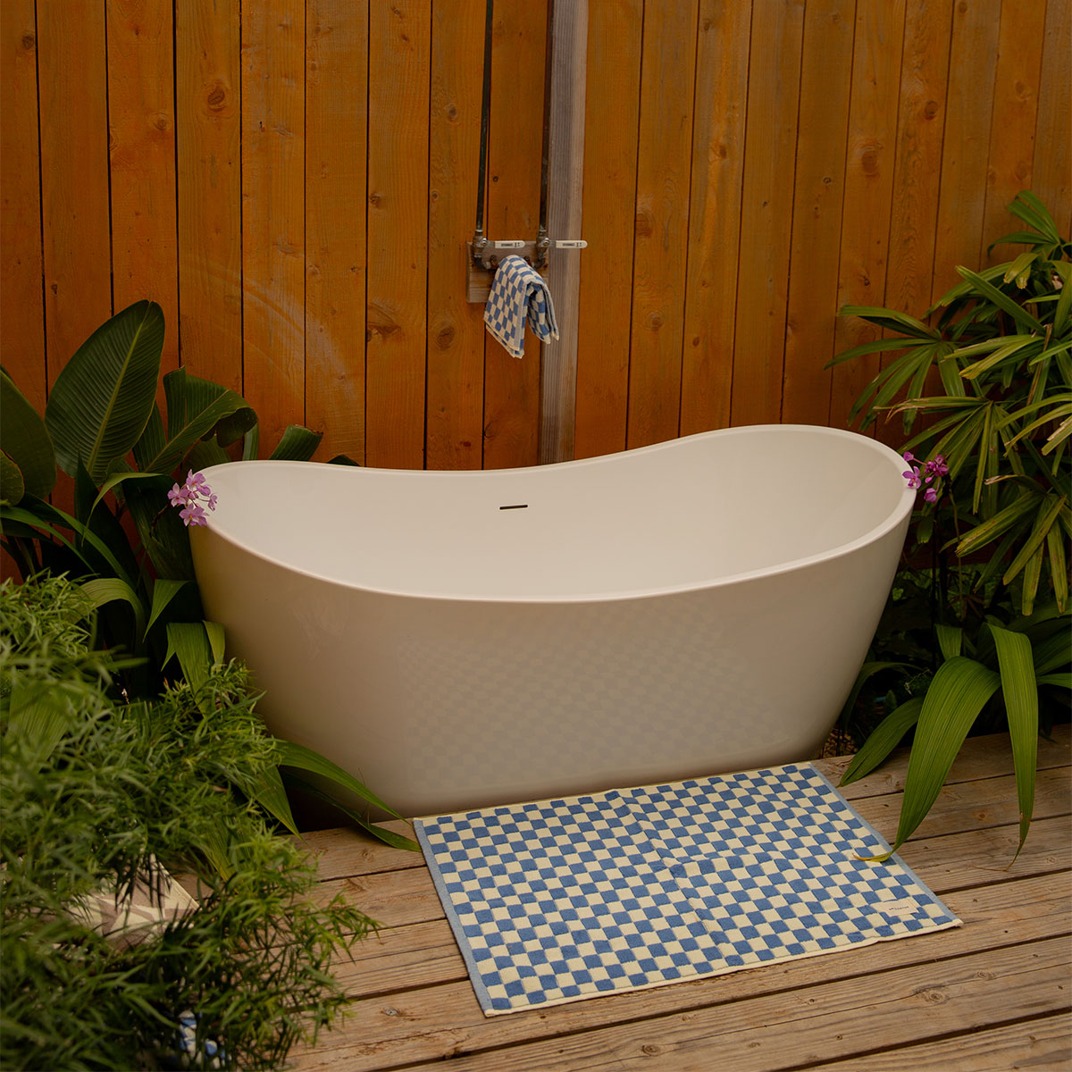 Cotton bath mat in blue and white checkered pattern on floor by white soaking tub.