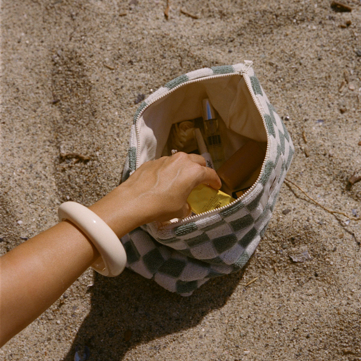 Travel pouch with toiletries on sand.