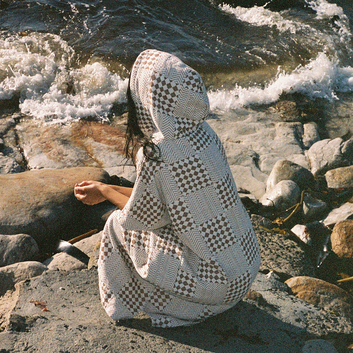 Surf poncho in brown and white checkered sustainable cotton by the water.