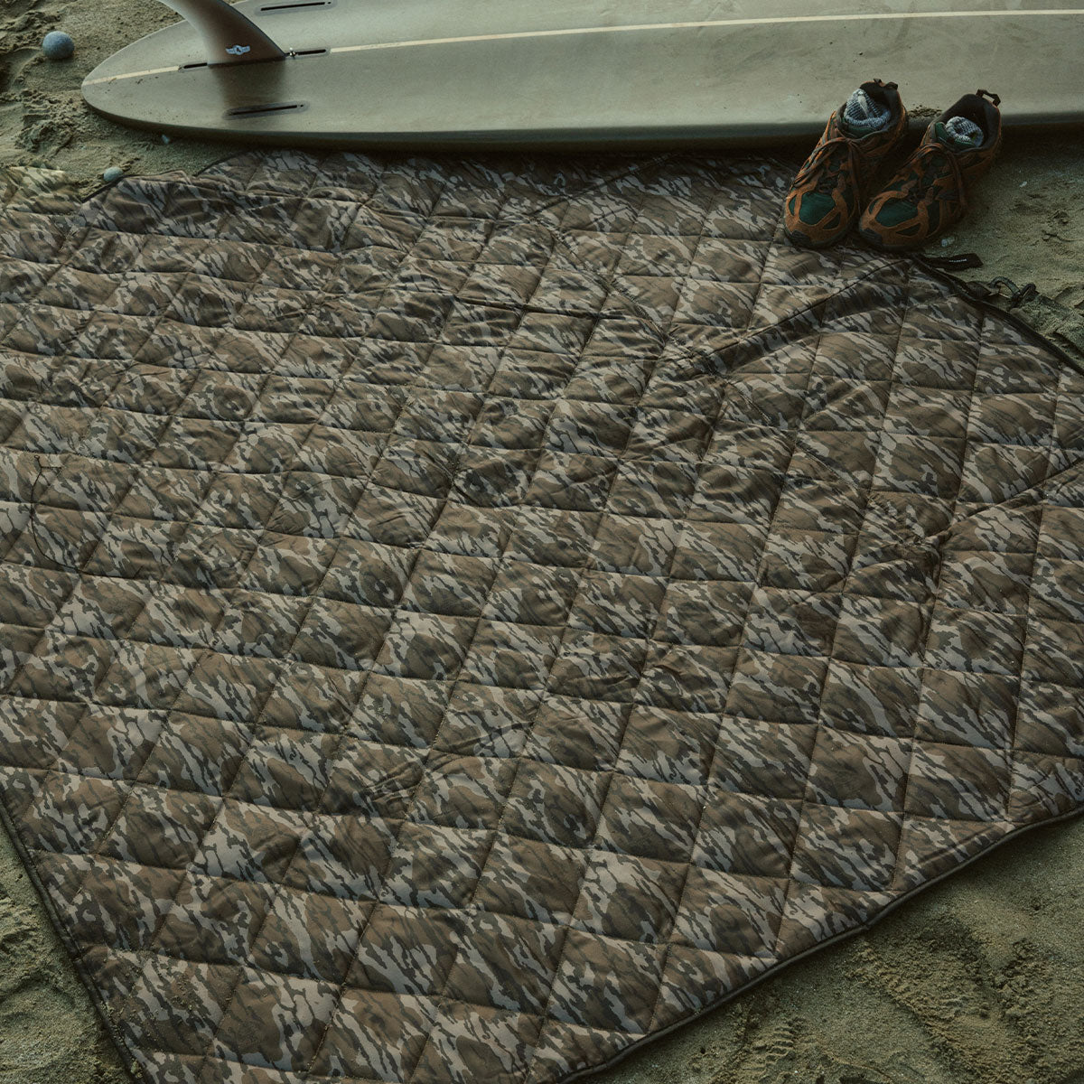 Quilted camouflage blanket on sand.