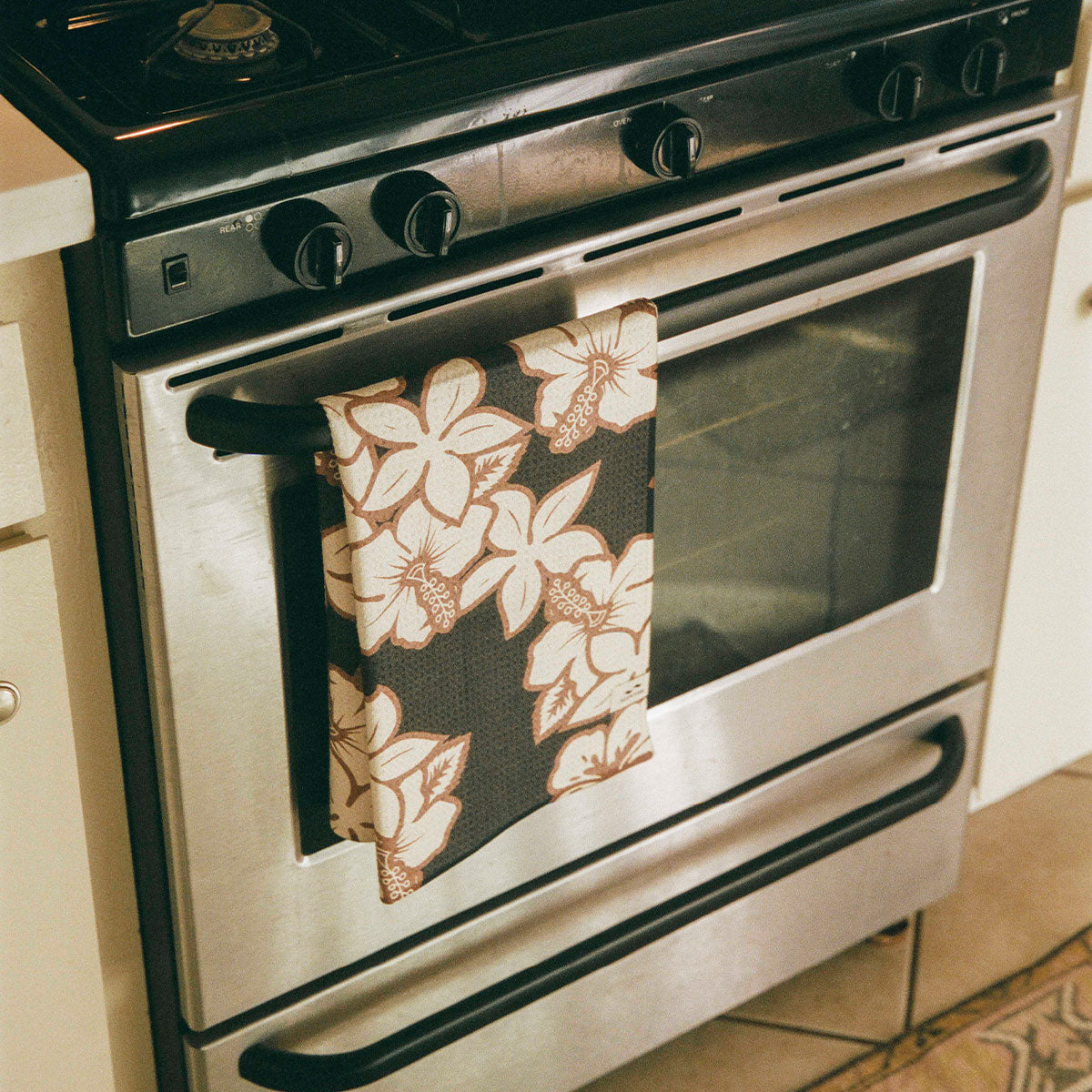 Quick dry towel with floral pattern hanging on stainless steel oven handle.