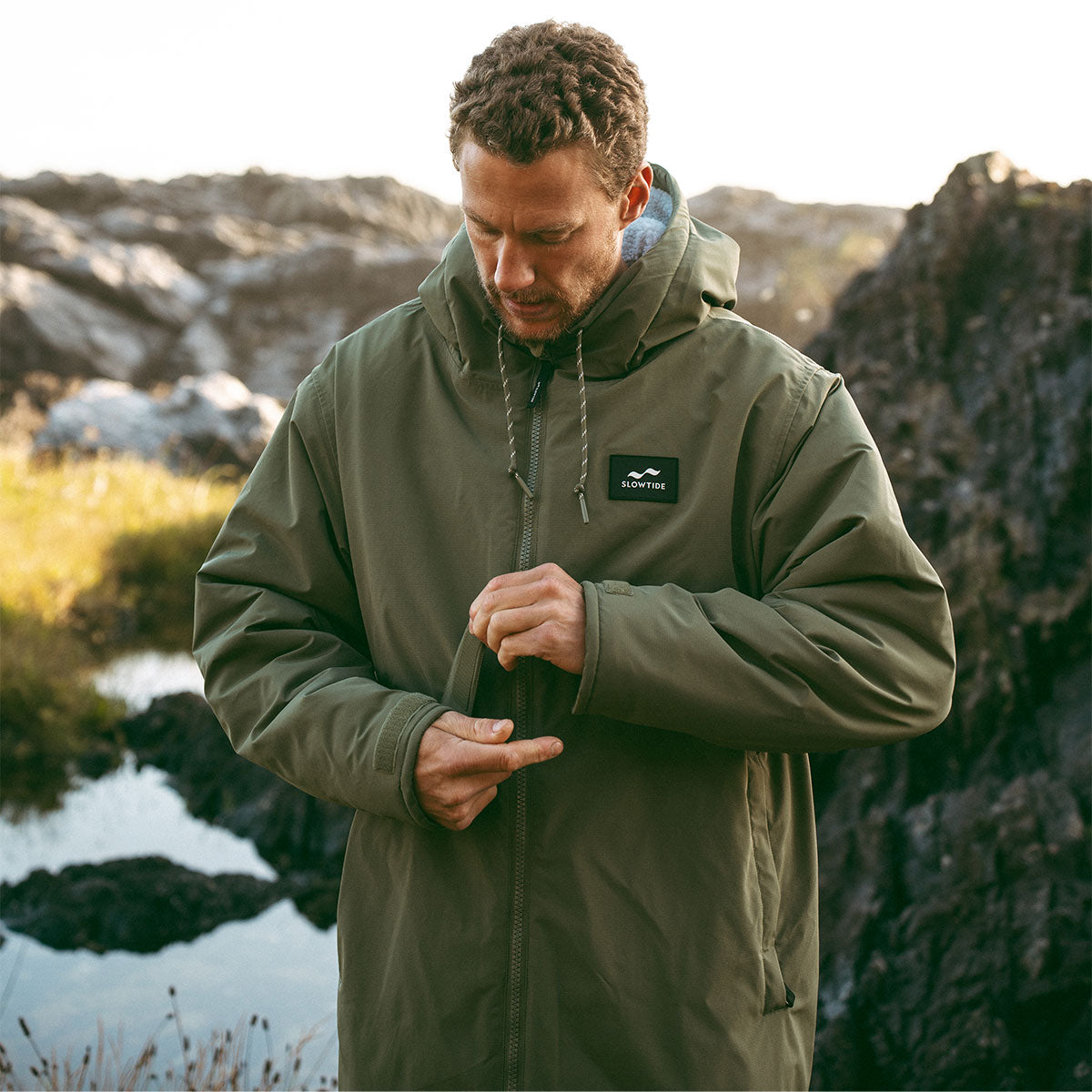 Green all-weather parka with front zipper closure, outdoor setting.