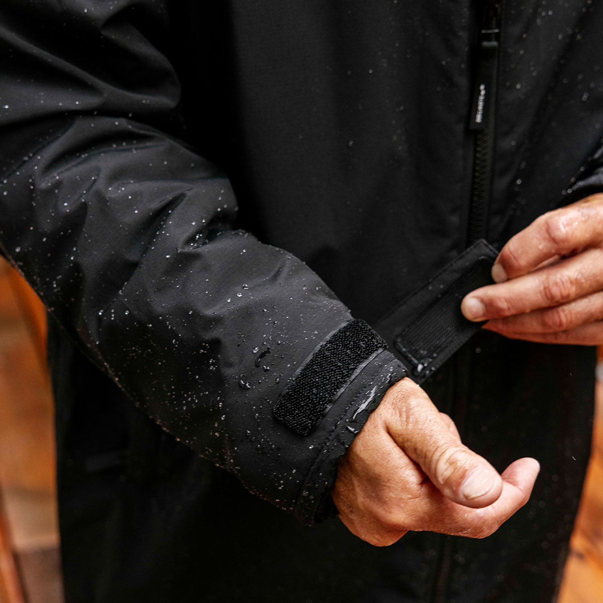 Black waterproof shell jacket sleeve with velcro strap, shown wet for water resistance.