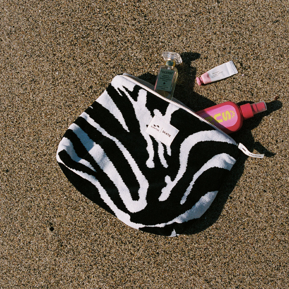 Zebra-striped terry pouch with partially visible cosmetics on sand.