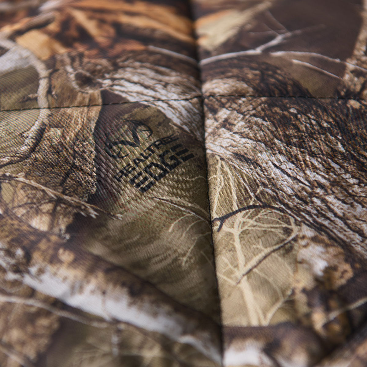Quilted packable blanket with photorealistic camo print and stitched logo detail.