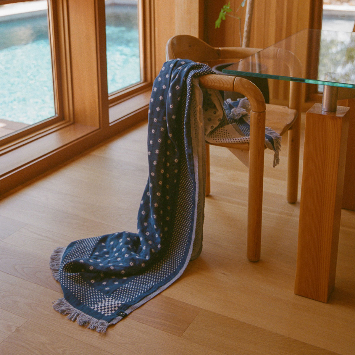 Lightweight blue scarf with pattern on wooden chair by window.