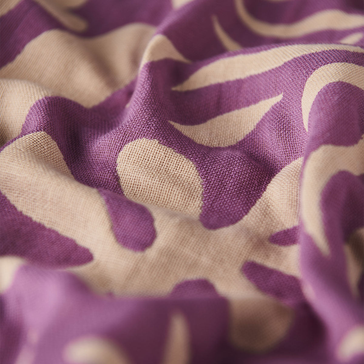 Fabric, lightweight beige with bold purple and cream botanical print, slightly wrinkled.