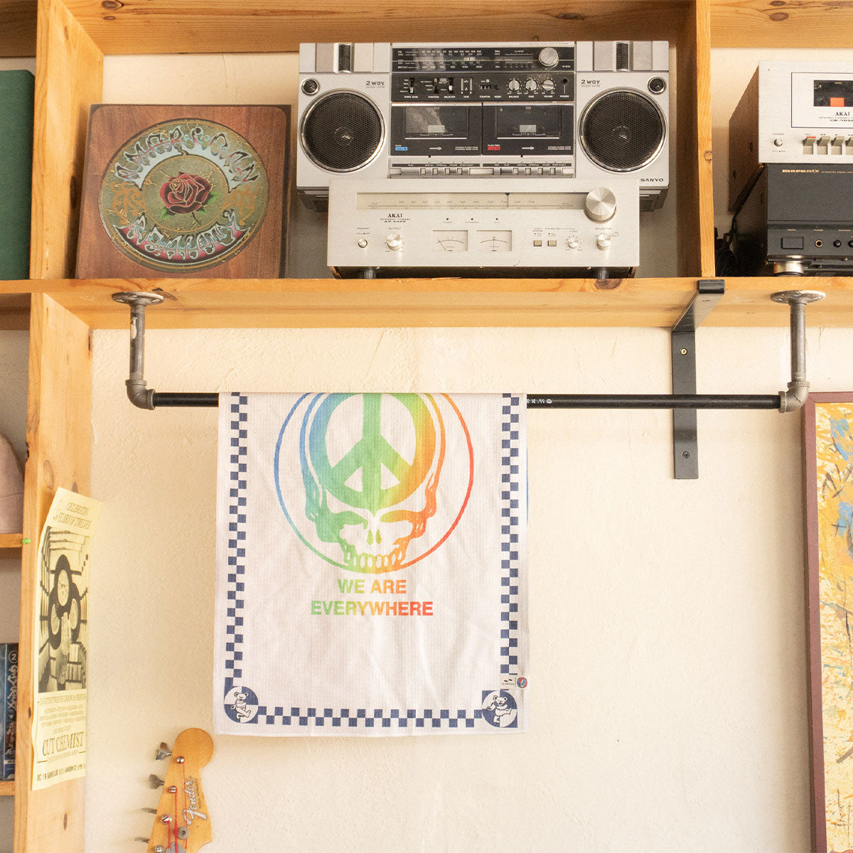 Kitchen towel with rainbow skull pattern hanging below stereo on a wooden shelf.