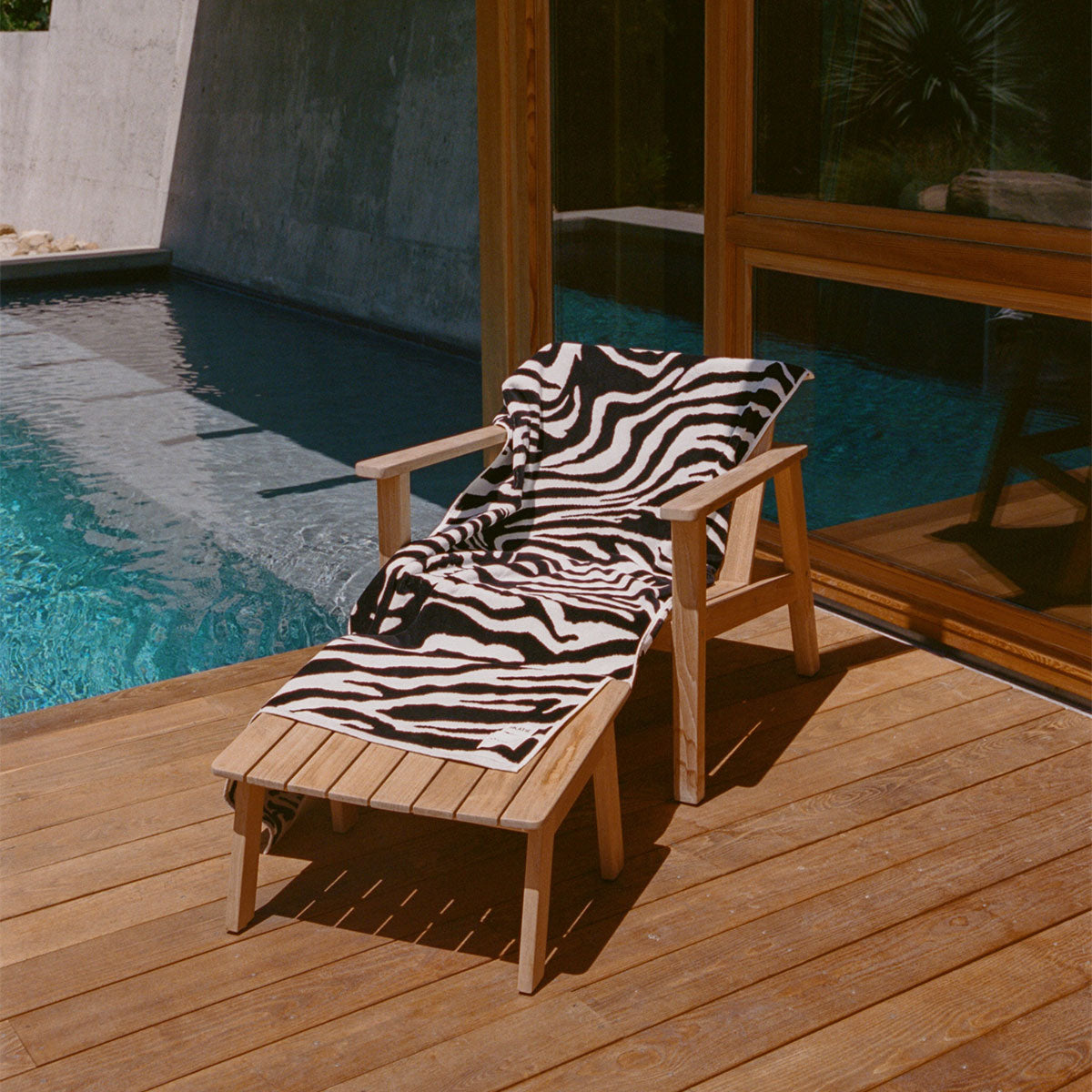 Wooden lounge chair with sustainable cotton towel on sunny poolside deck.