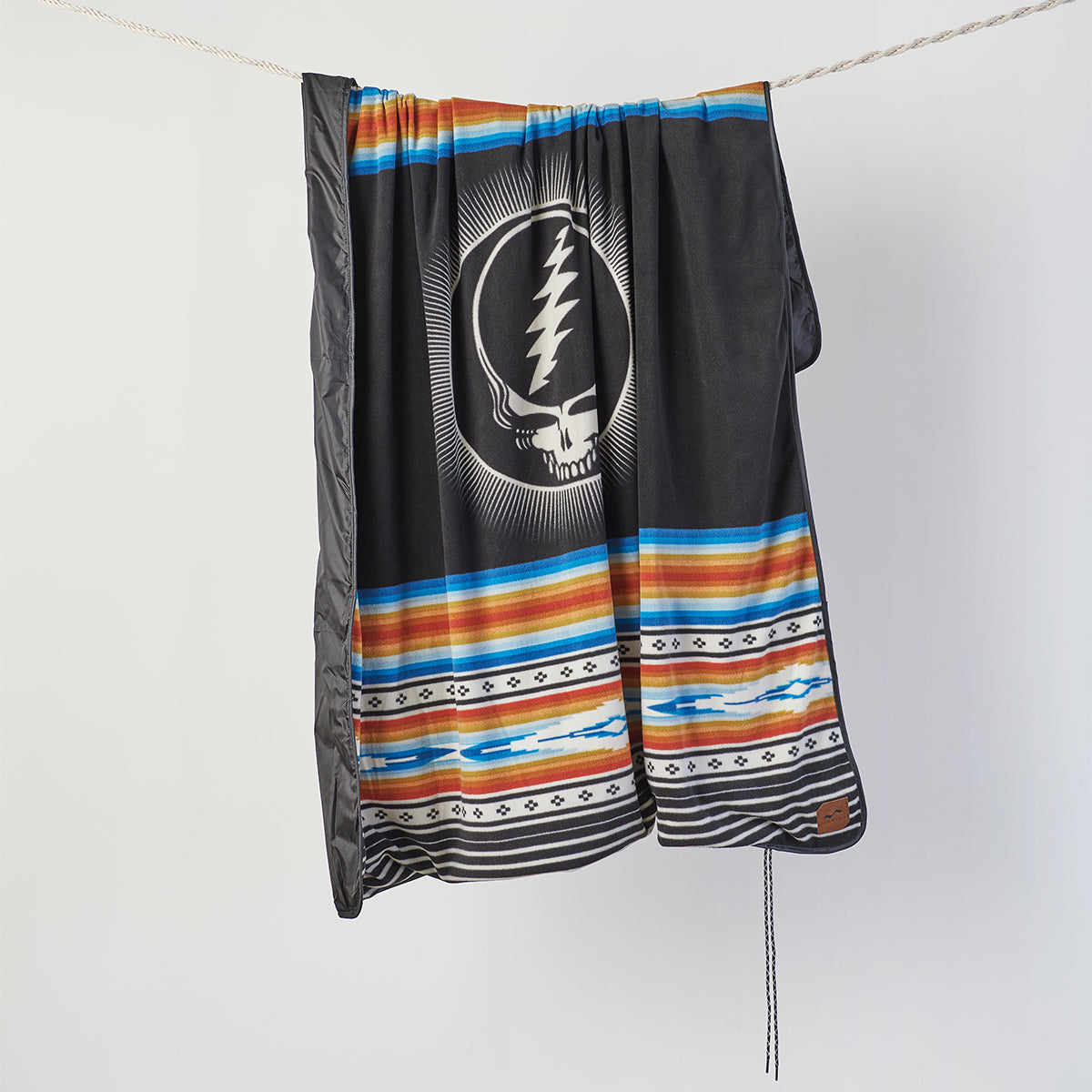 Water-repellent blanket with skull logo and colorful stripes hanging on a rope.