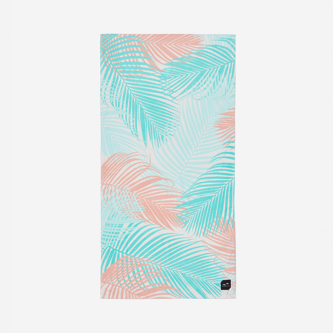 Beach towel with pastel pink and blue palm leaf pattern on white, sustainable material.