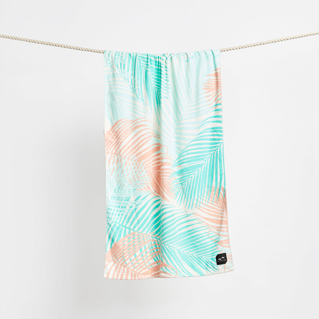 Beach towel, sustainable material, pastel palm leaf print, shown hanging on rope.
