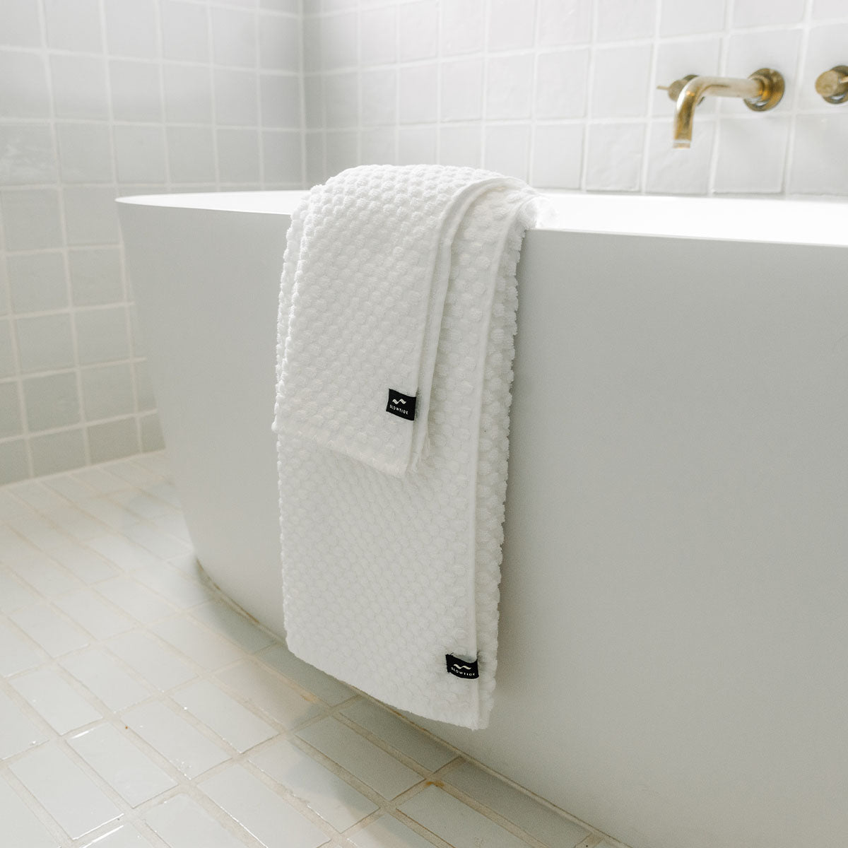 Spa towels, sustainably sourced cotton, draped on edge of white bathtub.