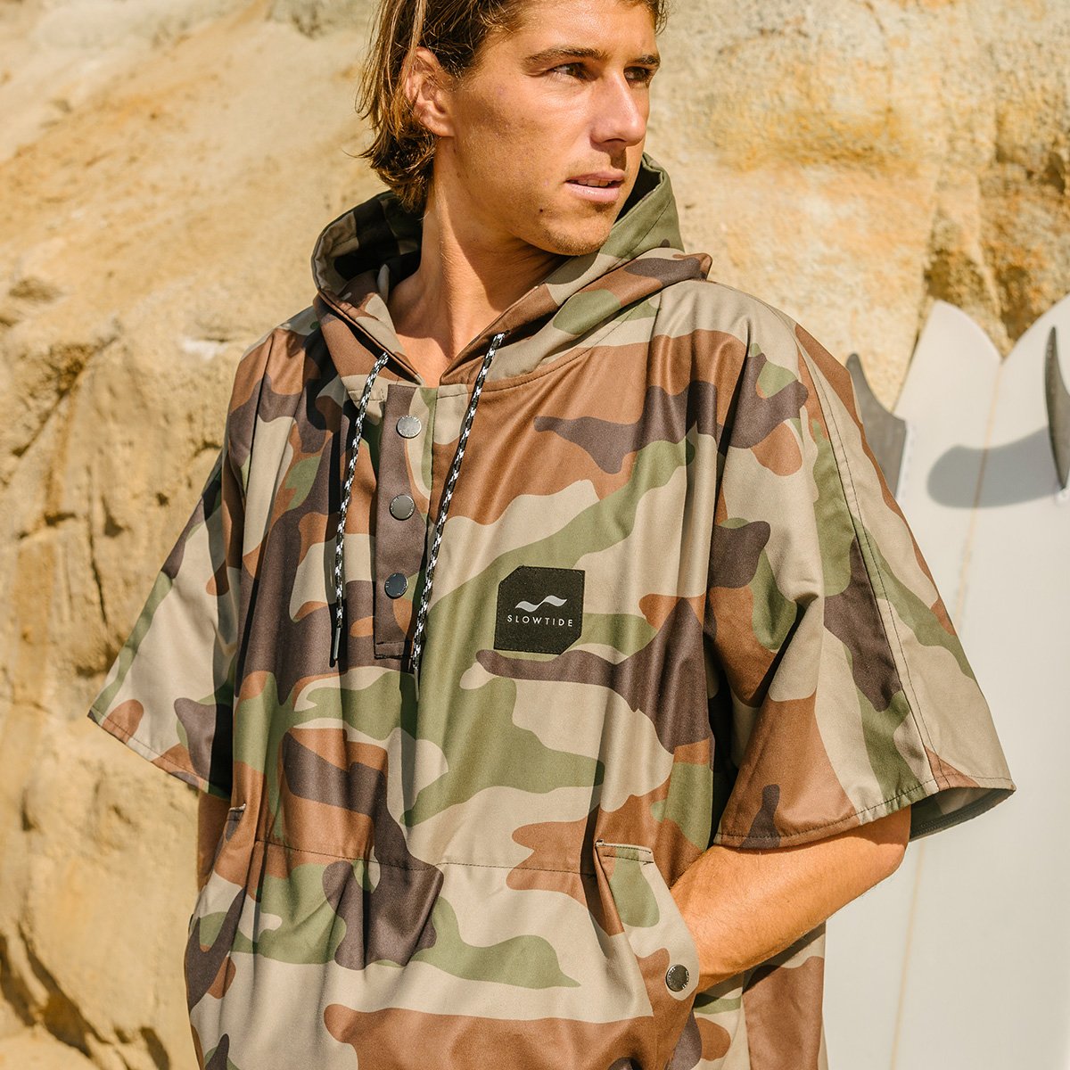 Camo quick-dry changing poncho with hood, outdoors near rocks and surfboard.