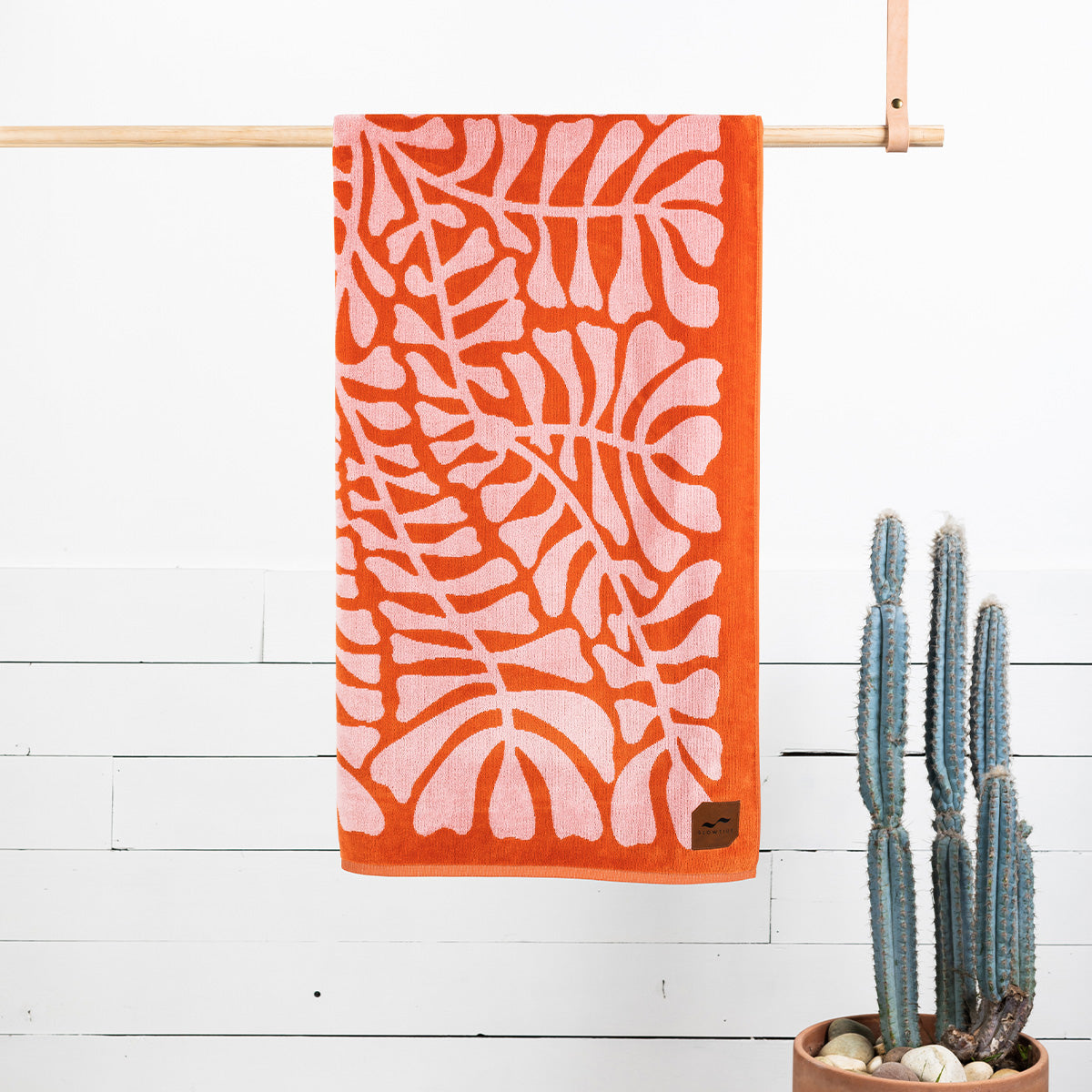 Jacquard beach towel in orange and pink with geometric pattern hanging indoors near cactus.