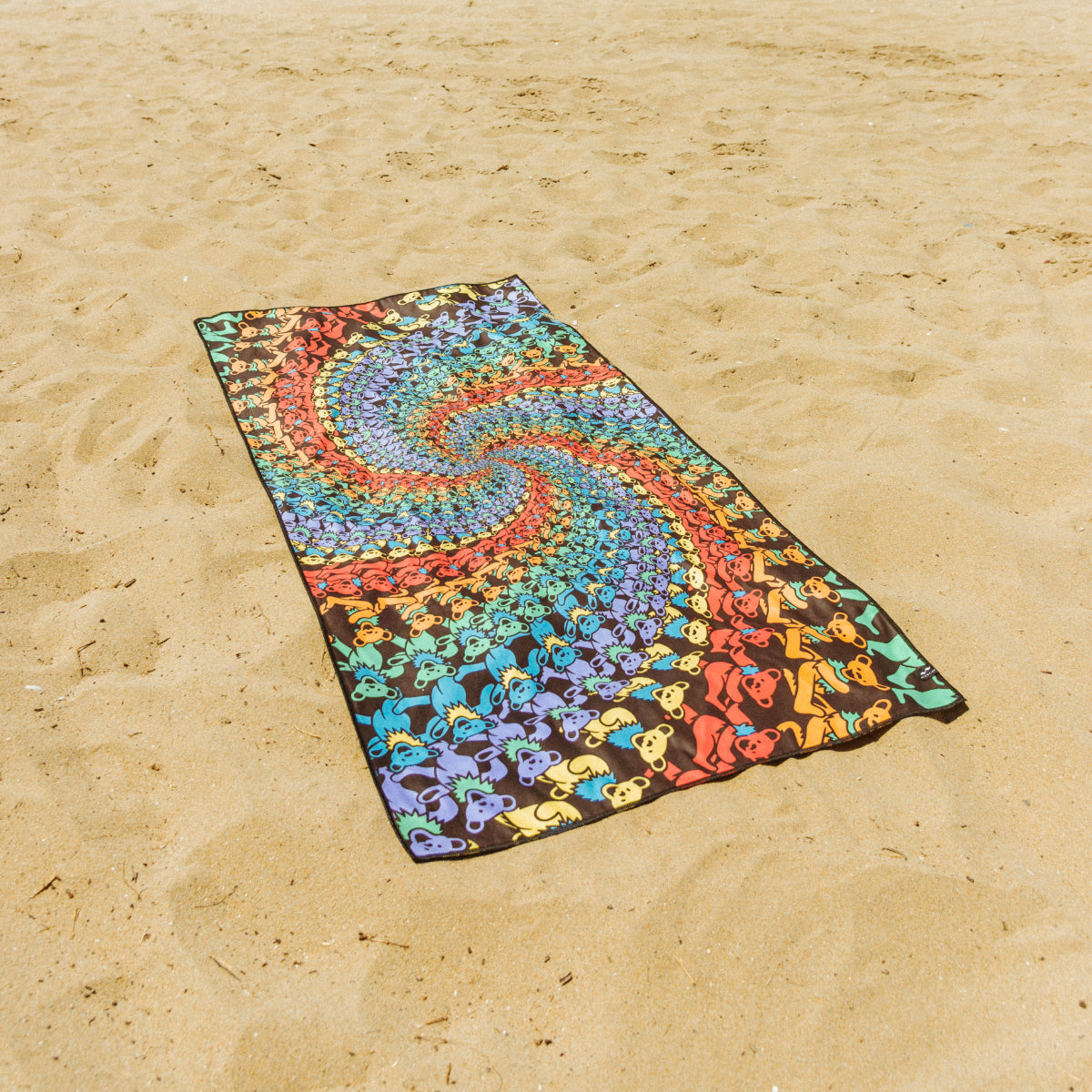 Sand-free towel with colorful psychedelic swirl and bear pattern on sandy beach.