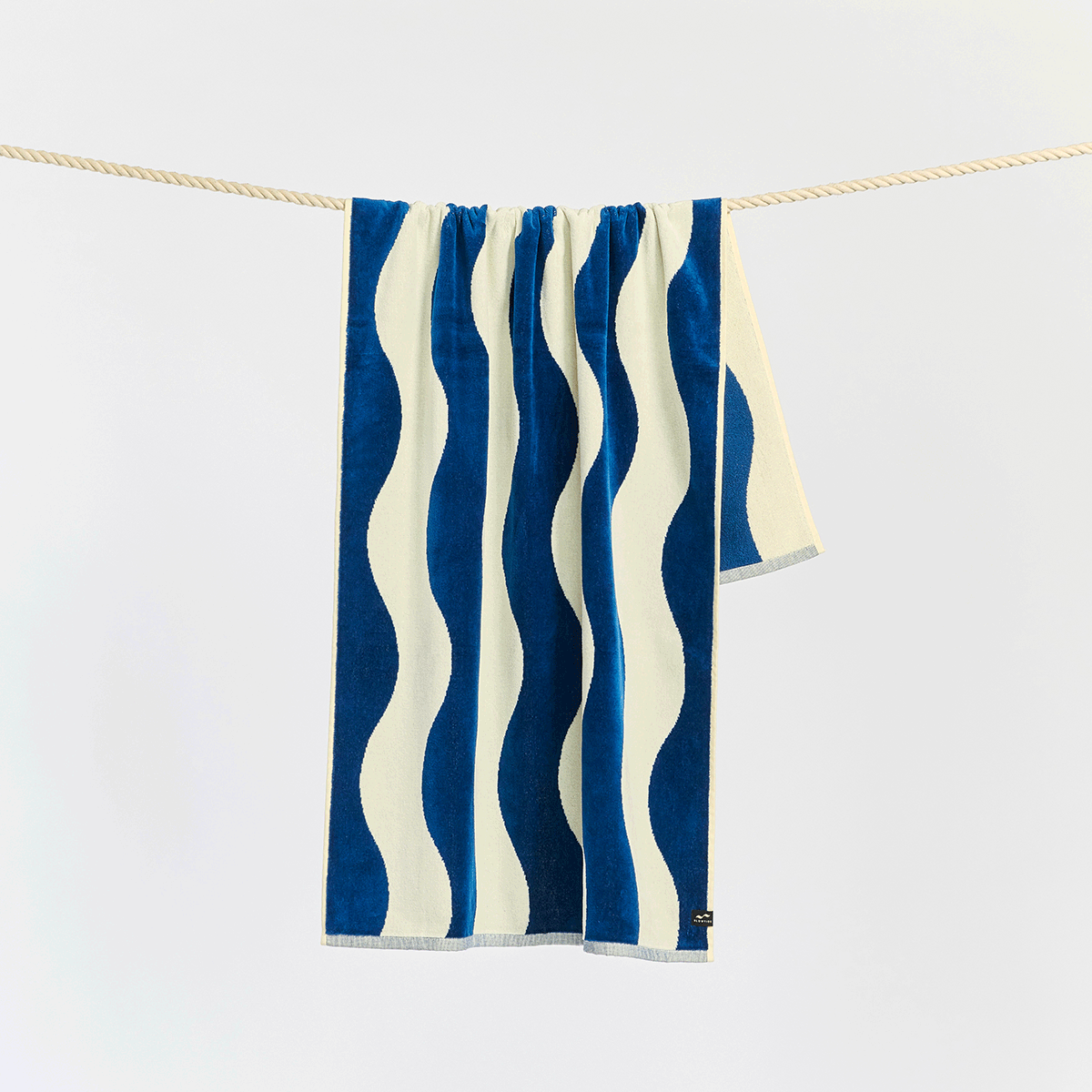 A towel with wavy blue and white stripes hangs neatly over a rope against a plain white background.