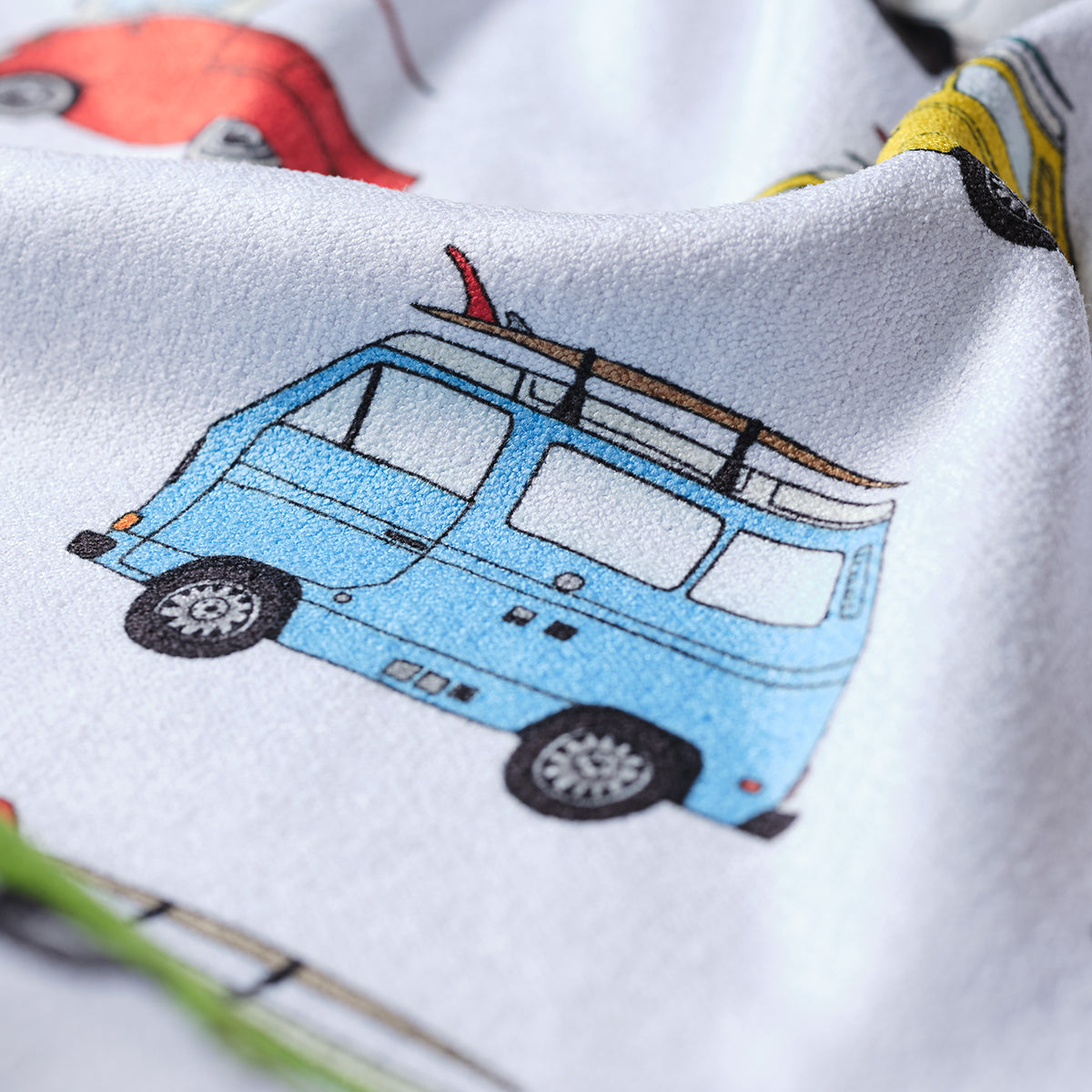 A close-up of fabric featuring colorful illustrations of vintage vans, including a prominent blue van with a roof rack and red surfboard, against a white background.