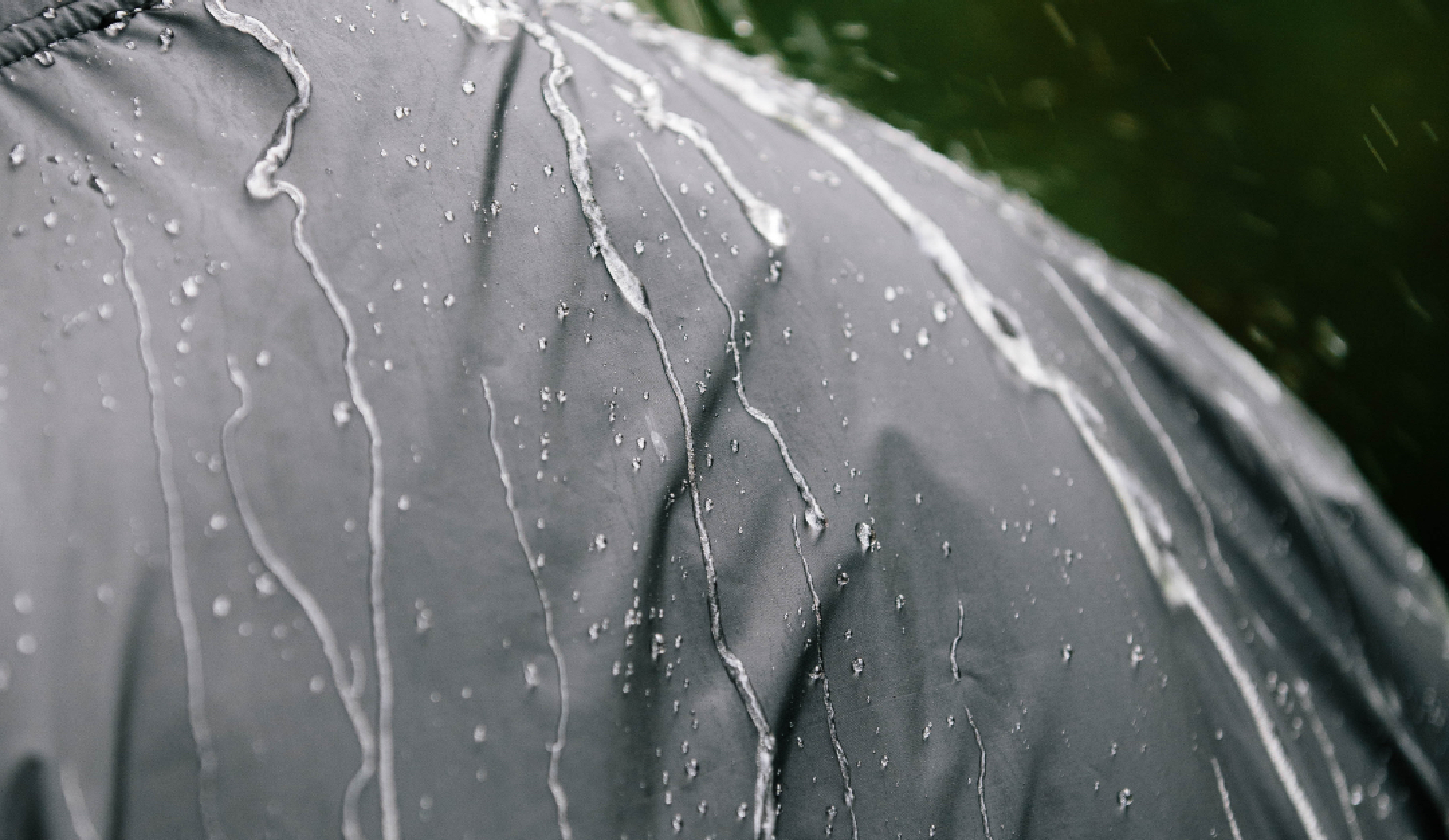 Close-up of water droplets and streams running down the surface of a gray waterproof jacket, demonstrating its water-resistant material.