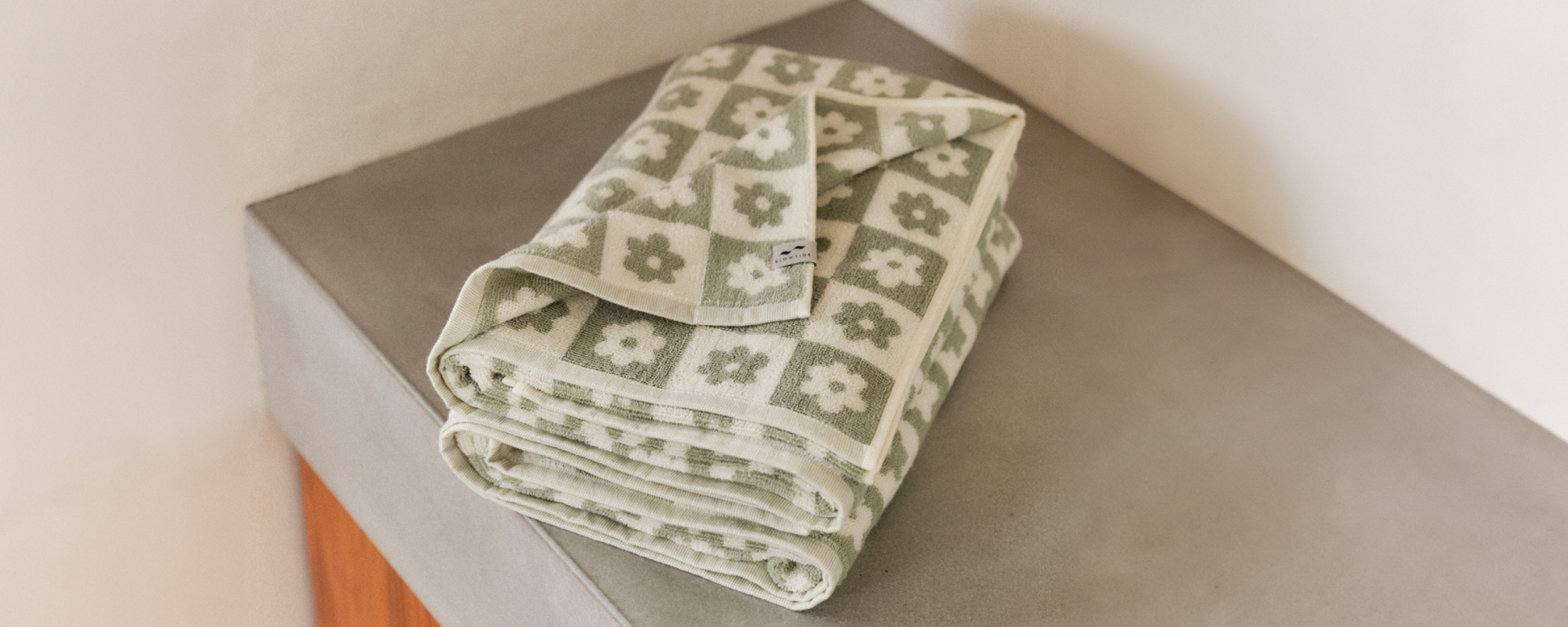 A folded green and white towel with a floral pattern rests on a smooth gray surface against a light-colored wall.