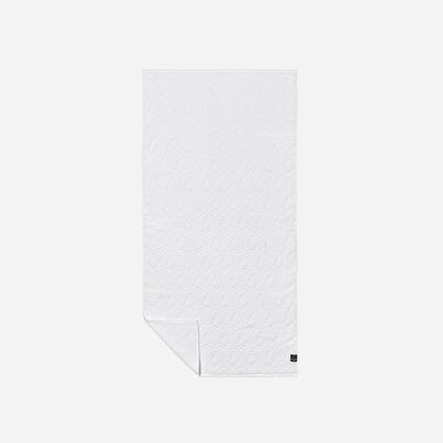 White dyeable bath towel with subtle textured pattern and small black corner tag.
