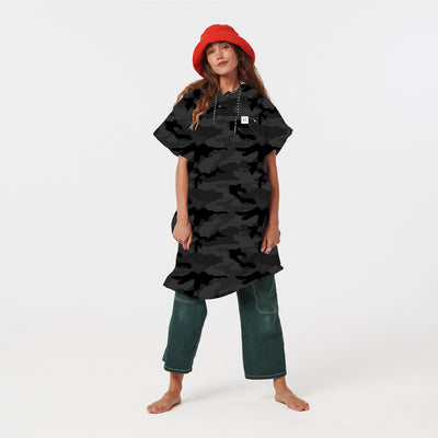 Oversized towel poncho with black camo shirt-dress and green jeans ensemble.