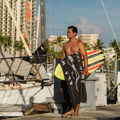 Quick-drying towel with surfboard, marina setting, sunlit day.