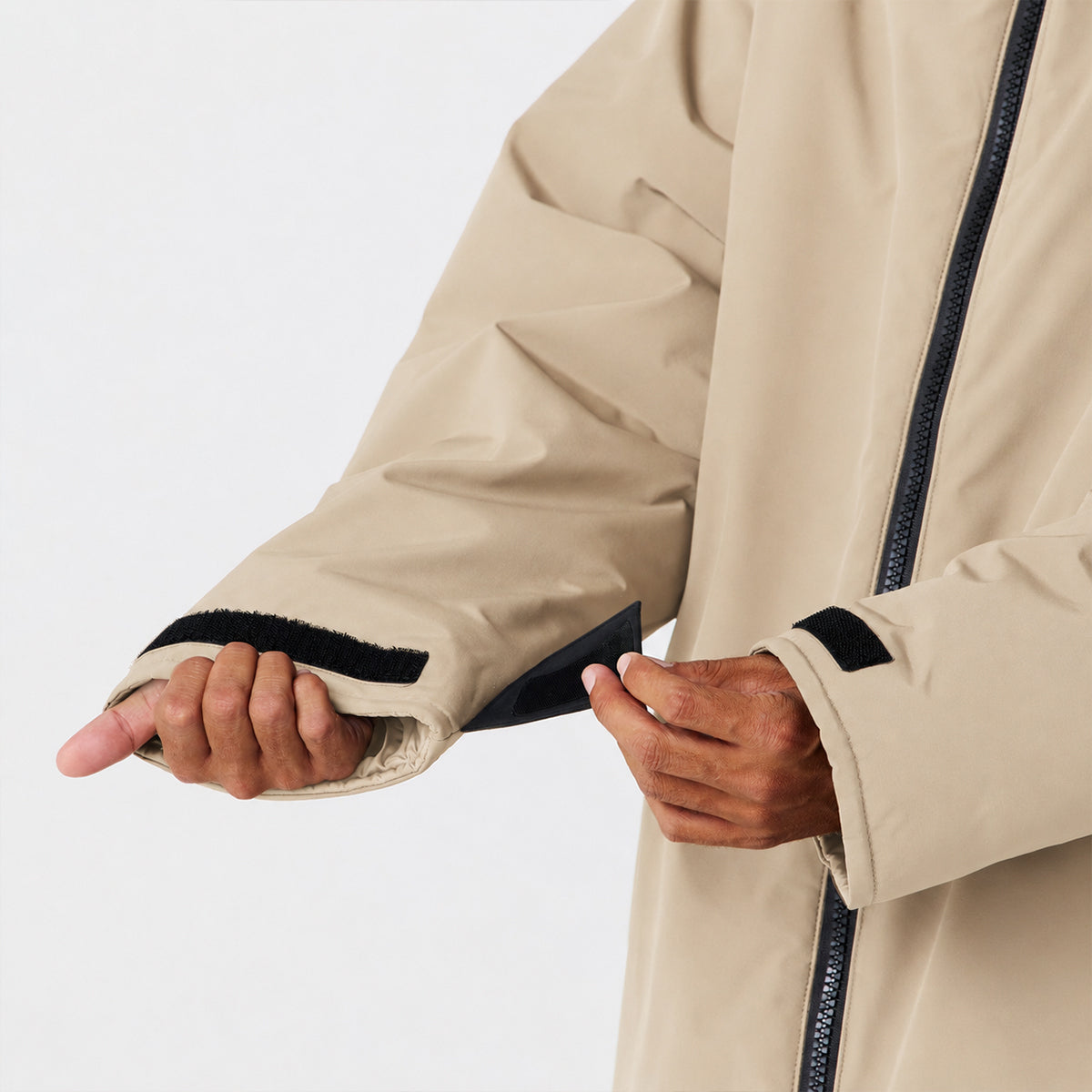 Beige waterproof parka with adjustable black velcro strap on sleeve for insulation.