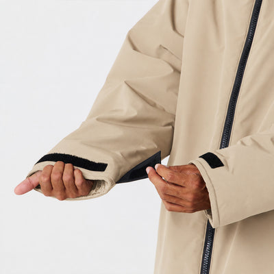 Beige waterproof parka with adjustable black velcro strap on sleeve for insulation.