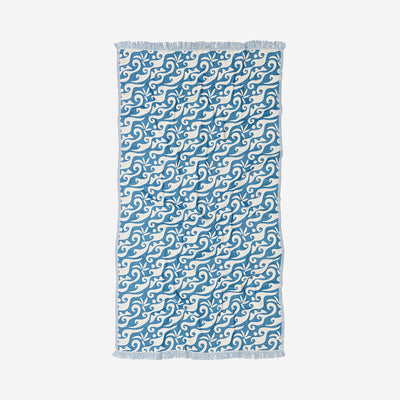 Beach towel with ocean blue swirling wave pattern and fringed edges for beach use.