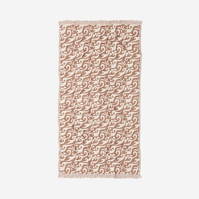 Beige cotton towel with white wave print and fringe on short edges.