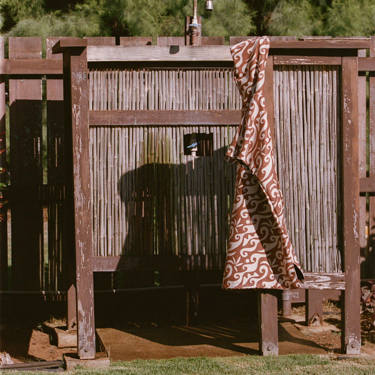 Wooden outdoor shower with patterned brown high-absorbency towel draped over side.