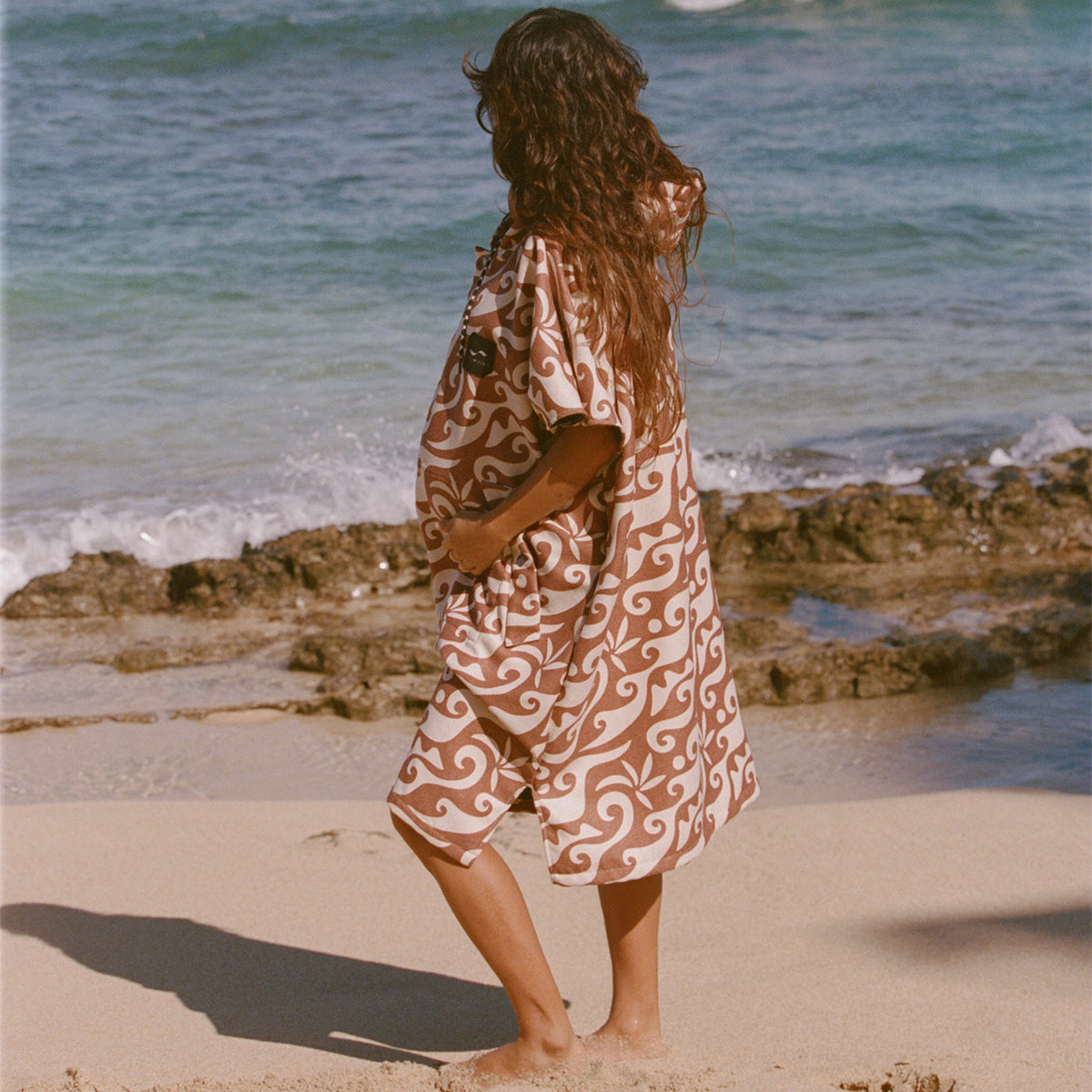 Changing poncho, recycled materials, patterned design, on sandy beach with ocean waves.