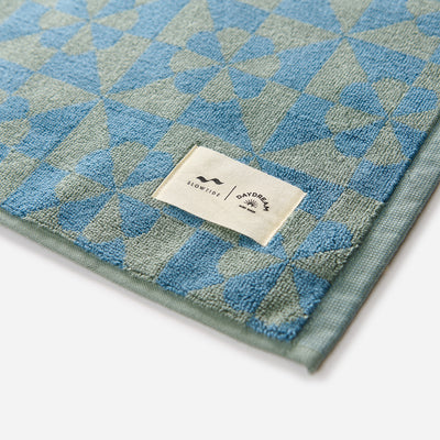 Dusty blue bath mat with white corner label, soft fabric, simple modern design.