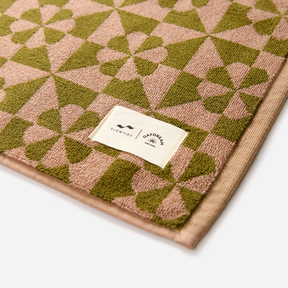 Bath mat with pink and green geometric texture, white fabric label on corner.