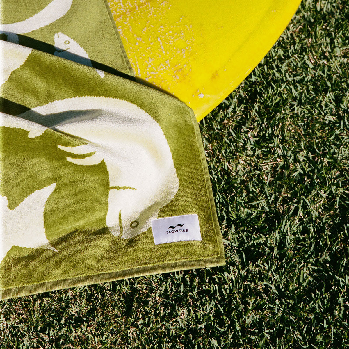 Beach towel, cotton, green and white fish pattern, displayed on grass near yellow item.