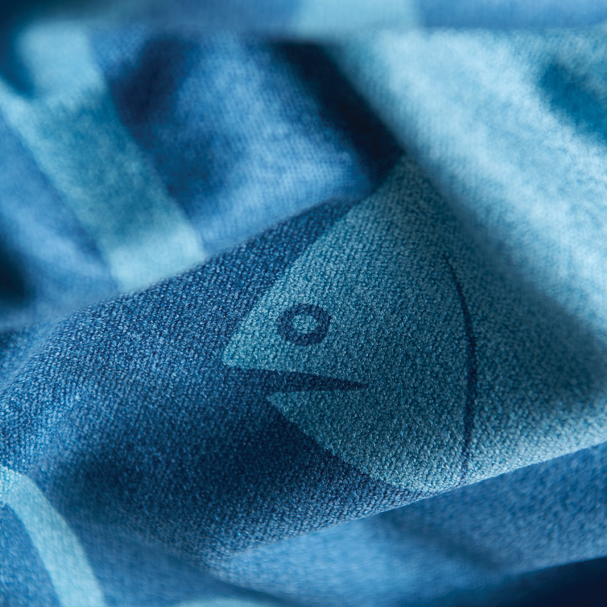 Blue recycled towel with fish illustration and soft folds, close-up product detail.