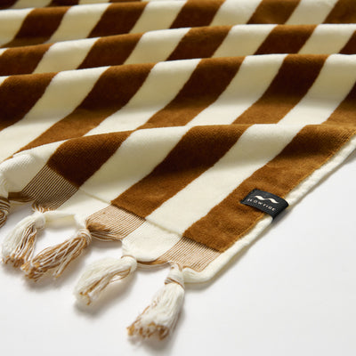 Cotton blanket with brown and white stripes, tassels, and a small black edge tag.