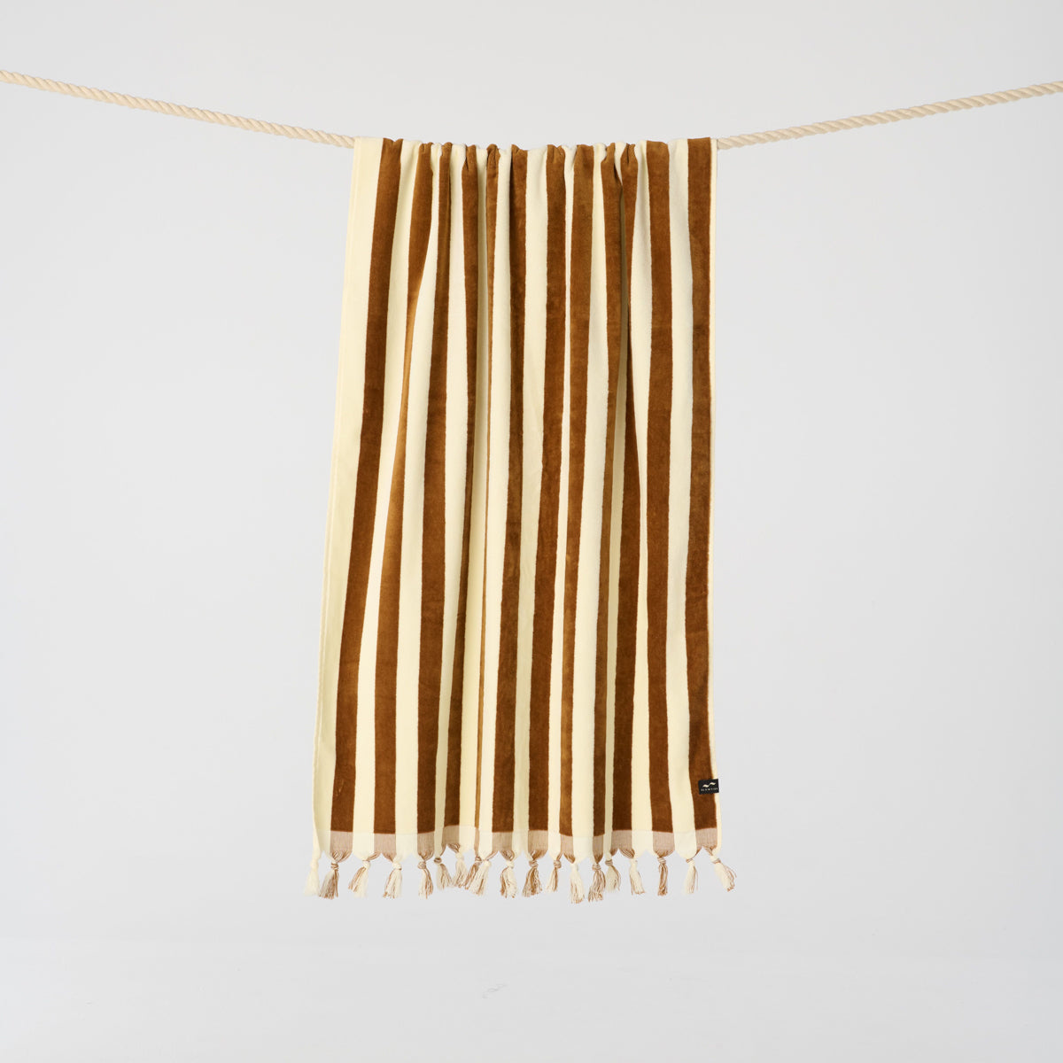Woven towel with beige and brown stripes, fringed edges, hanging on a rope.