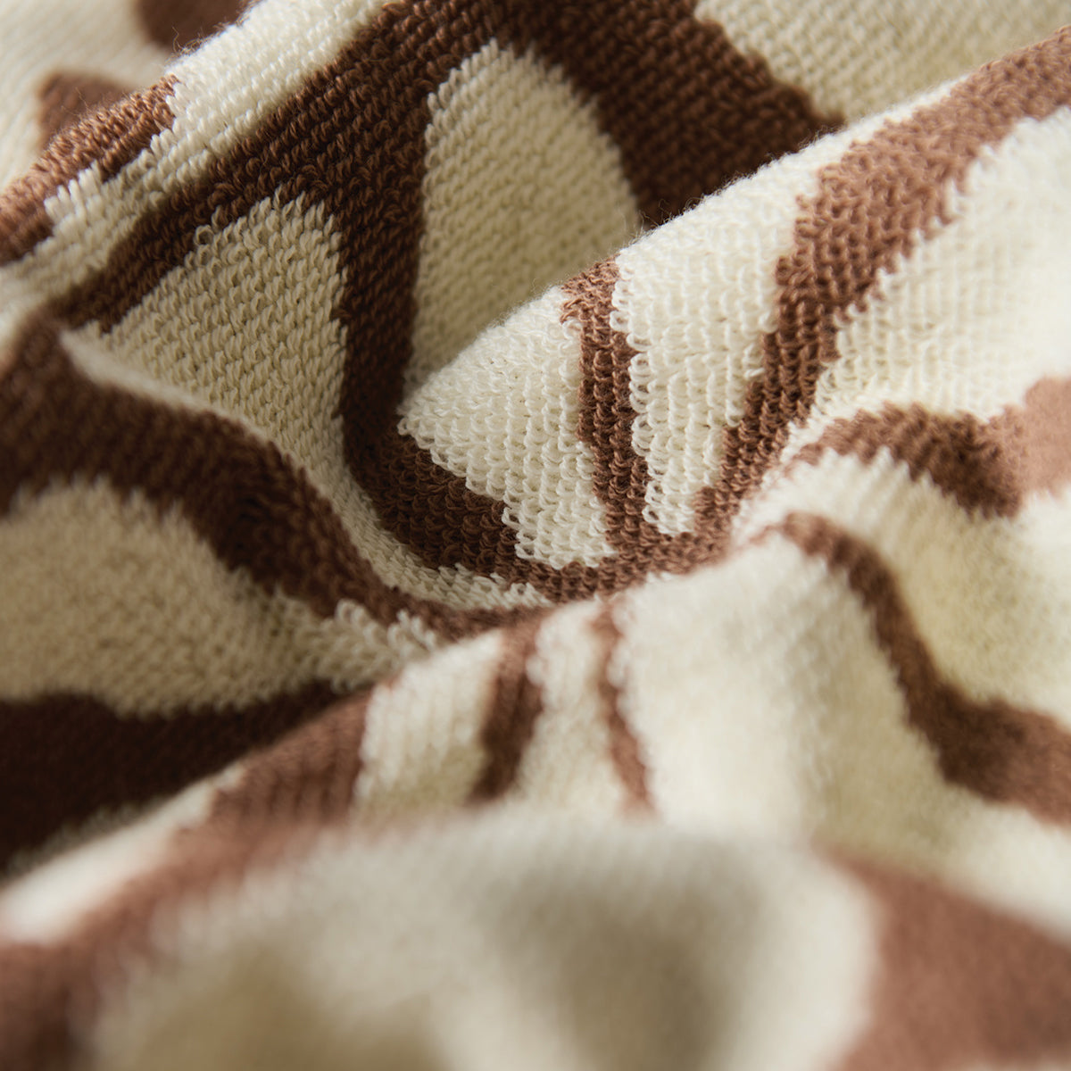 Hand towel, cotton, beige and brown geometric sun-like pattern, close-up view.