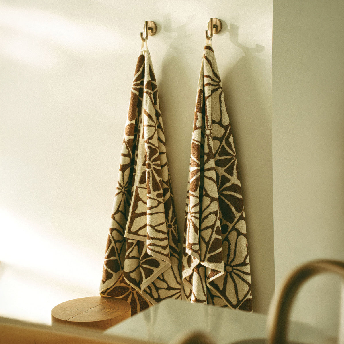 Absorbent bath towels with brown and cream floral pattern hanging on wall hooks.