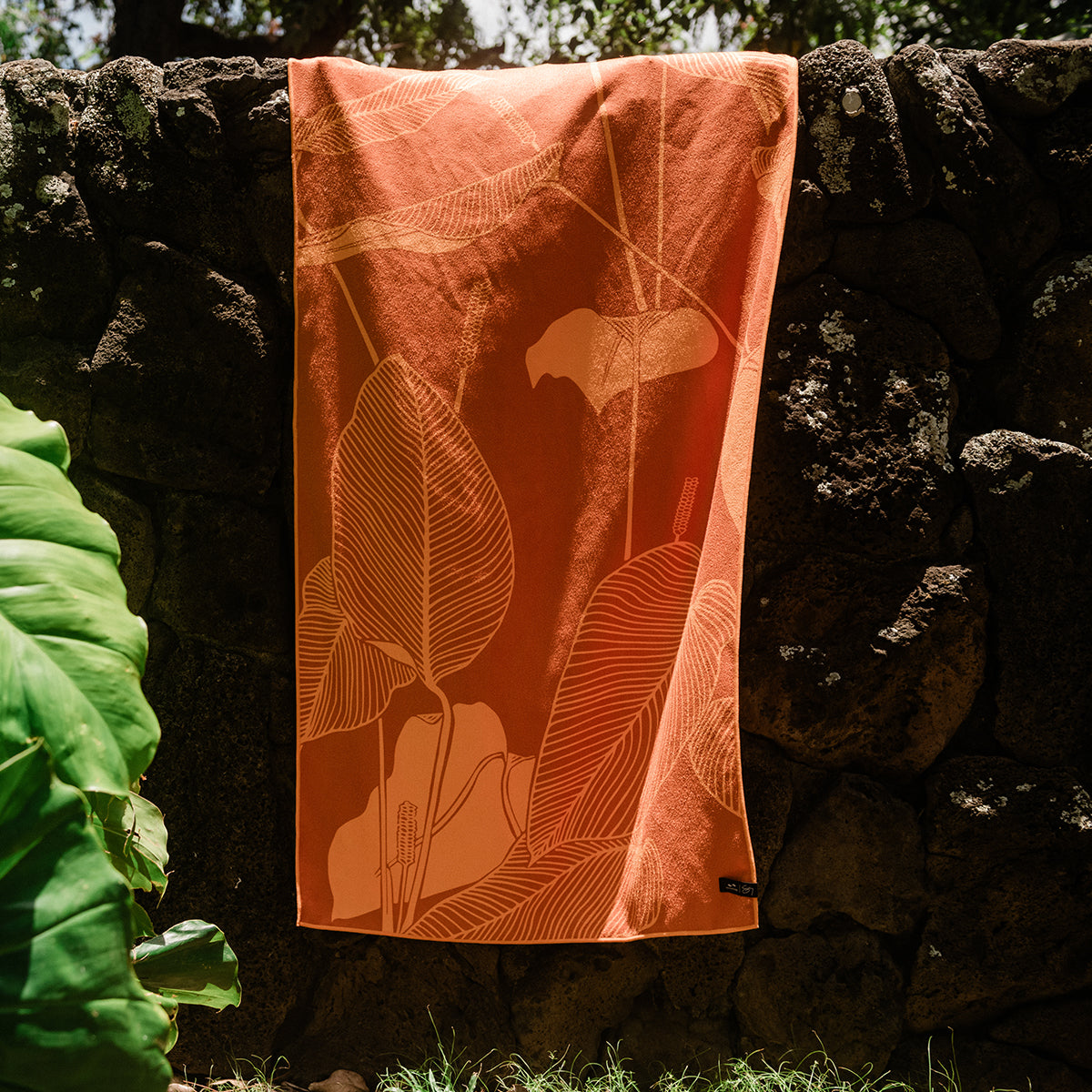 Towel with leaf pattern on stone wall in sunlight.