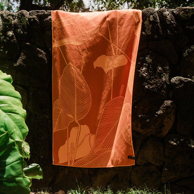 Towel with leaf pattern on stone wall in sunlight.