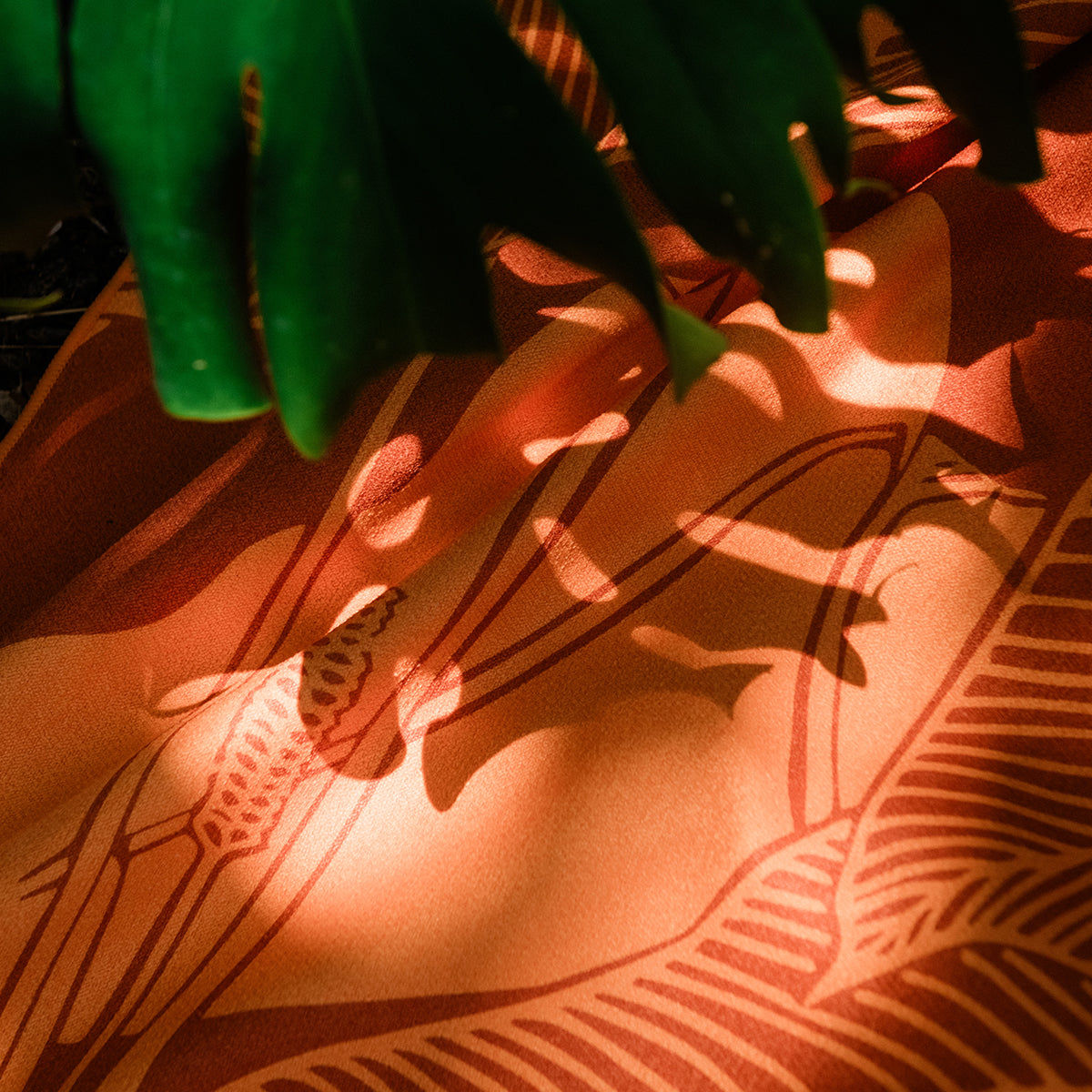 Textile with orange and brown geometric pattern, sunlight dappling through green leaves.