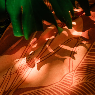 Textile with orange and brown geometric pattern, sunlight dappling through green leaves.