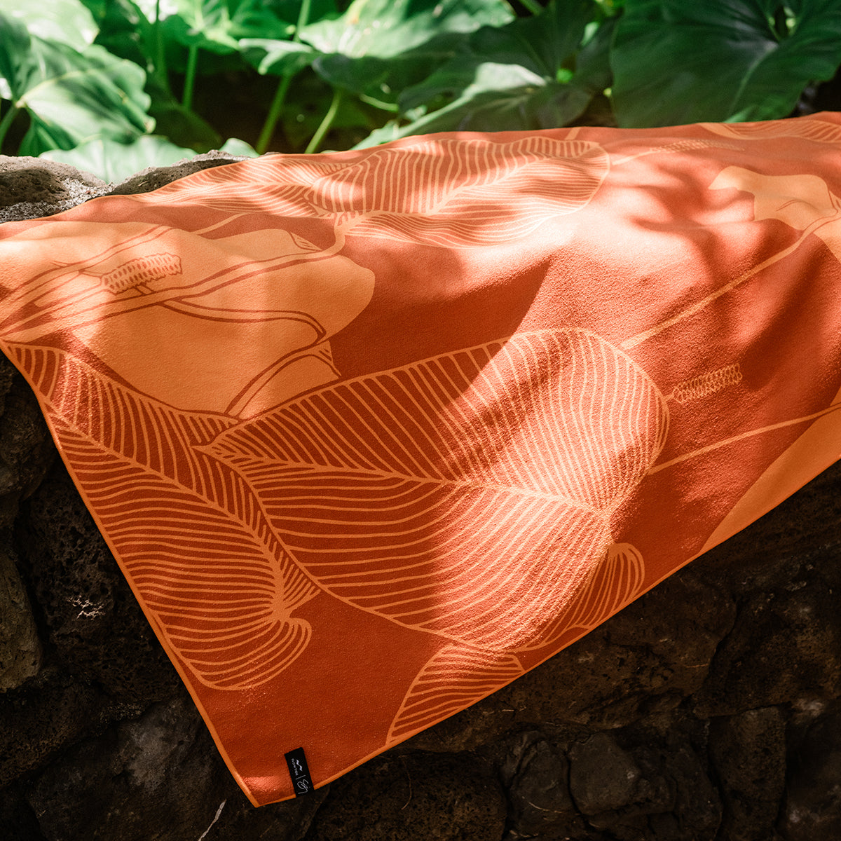 Towel with leaf pattern draped on stone wall.