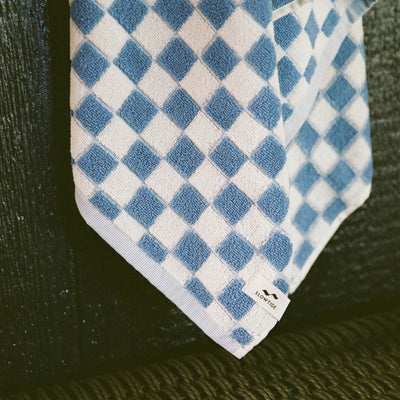 Cotton terry bath towel with blue and white checkerboard pattern on dark surface.