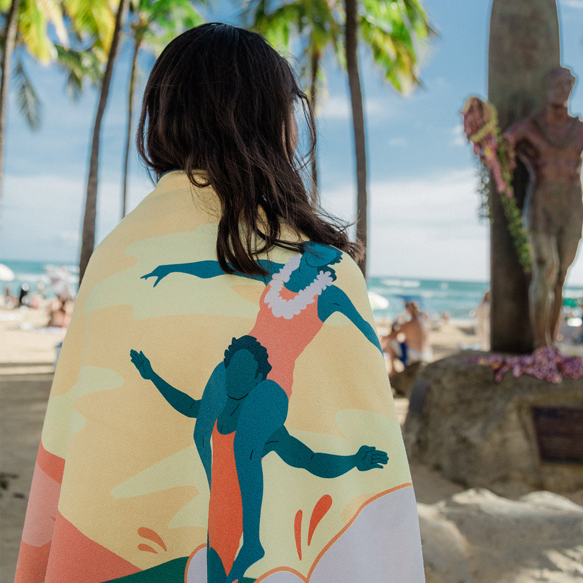 Quick-drying microfiber towel with colorful surfer pattern on the beach.