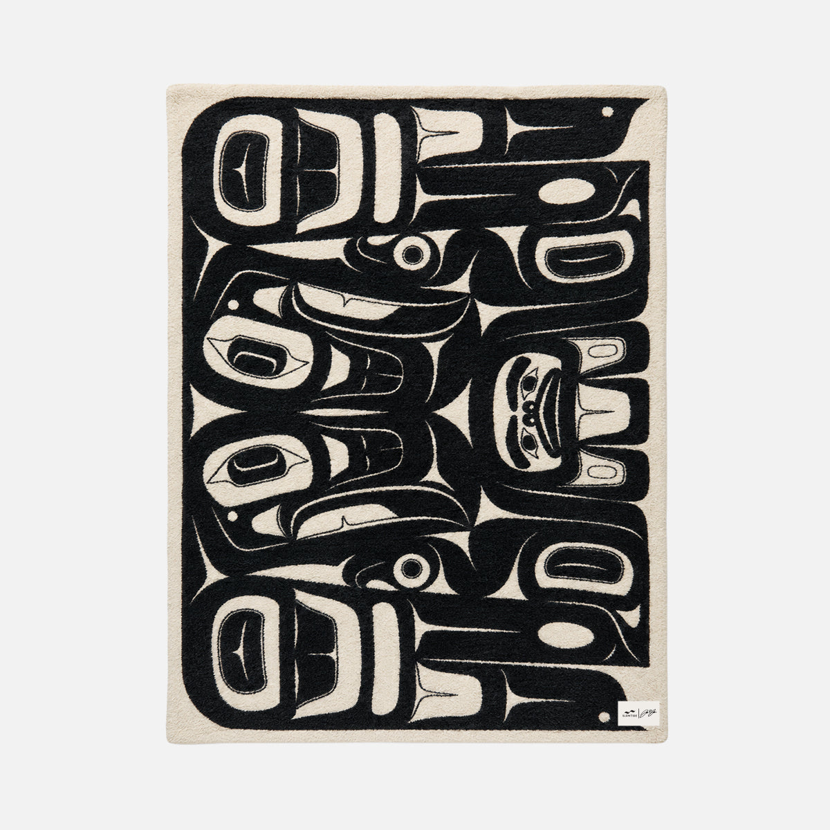 Plush reversible throw with black and white Indigenous-inspired animal pattern.